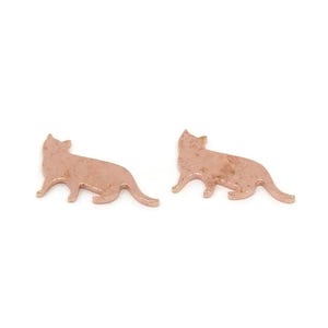 May include: Two rose gold cat-shaped charms. Each charm is a silhouette of a cat in a walking pose, with a textured surface. The charms are displayed on a white background.