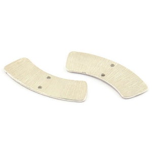 May include: Two silver metal pieces shaped like a crescent moon with two holes in each piece.