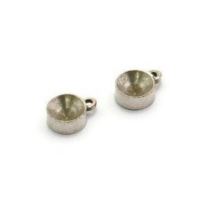 May include: Two silver-toned metal pendant settings with a round, concave top and a small loop for attaching a chain or cord.