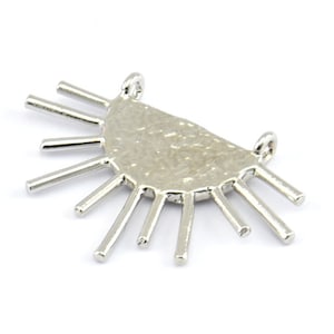 May include: Silver pendant with a half-circle design and a textured surface. The pendant has a series of thin, pointed metal prongs radiating out from the half-circle.