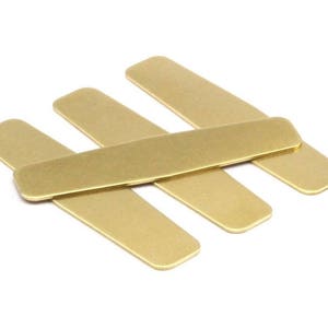 May include: Four gold-colored metal collar stays, stacked on top of each other. The collar stays are rectangular in shape and have a smooth, polished finish.