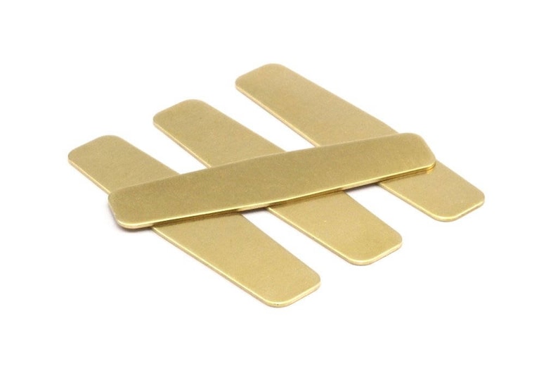 Puede incluir: Cuatro soportes de cuello de metal de color dorado, apilados uno encima del otro. Los soportes de cuello son de forma rectangular y tienen un acabado liso y pulido.
