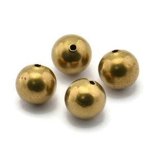 May include: Four gold-colored metal beads with a hole in the center. The beads are round and smooth.
