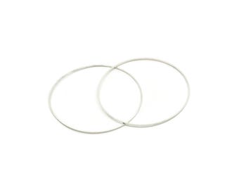 May include: Two thin, circular silver-toned metal hoops are positioned overlapping each other. The rings have a smooth, polished finish and a simple, continuous wire design, creating a clean and minimalist geometric shape.