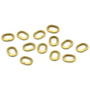 May include: A group of 14 gold oval jump rings. The rings are all the same size and are arranged in a random pattern on a white background.