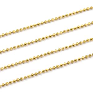 May include: Four strands of gold ball chain, a type of jewelry chain, are laid out in parallel lines on a white background.