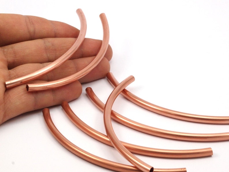 May include: A set of six copper pipe segments, each bent into a half-circle shape. The segments are arranged in a fan-like pattern, with the ends of the segments overlapping.