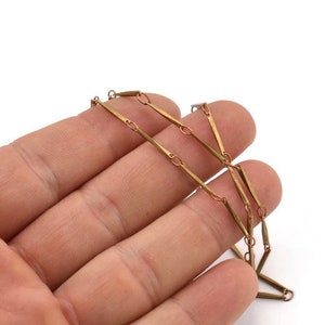 May include: A gold chain necklace with a unique design featuring long, thin, rectangular links connected by smaller, round links.