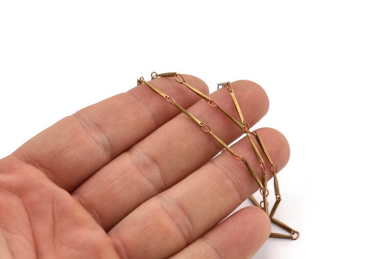 May include: A gold chain necklace with a unique design featuring long, thin, rectangular links connected by smaller, round links.