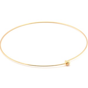 Könnte beinhalten: Ein schlichtes goldenes Armreif-Armband mit einem kleinen, runden, goldenen Verschluss.