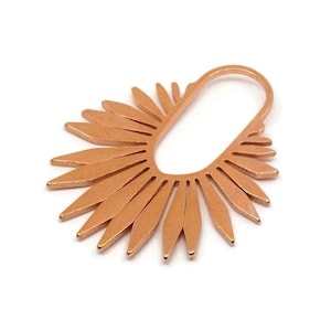 May include: A copper-coloured metal pendant with a sunburst design. The pendant has a central oval shape with radiating petal-like elements. The design is open, with a loop at the top for hanging.