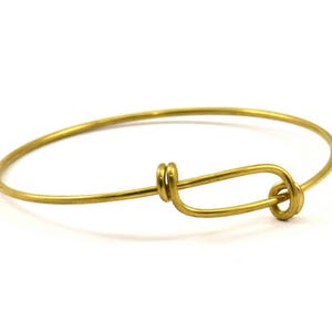 May include: A gold-toned bangle bracelet with a simple knot closure.