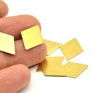 K&ouml;nnte beinhalten: Eine Gruppe kleiner, goldfarbener, rautenf&ouml;rmiger Metallst&uuml;cke. Die St&uuml;cke liegen auf einer wei&szlig;en Oberfl&auml;che verstreut und eine Hand h&auml;lt zwei der St&uuml;cke.