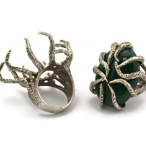 Könnte beinhalten: Zwei silberne Ringe mit einem detaillierten, organischen Design. Ein Ring hat einen grünen Edelstein.