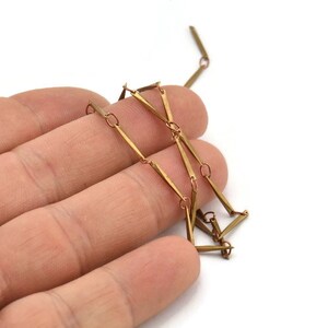 May include: A gold-toned chain necklace made of linked rectangular bars. The chain is lying on a hand.