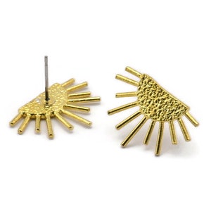 May include: A pair of gold-toned earrings with a sunburst design. Each earring features a half-circle shape with textured details and radiating lines.