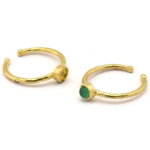 Könnte beinhalten: Zwei goldene Ringe mit einem grünen Edelstein. Die Ringe sind schlicht und zart, mit einer gehämmerten Oberfläche.