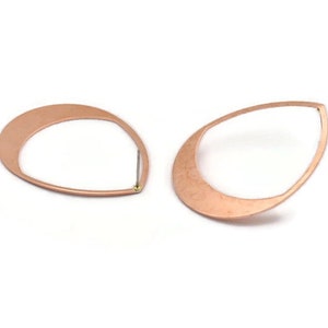 Op de afbeelding: Twee open oorbellen in de vorm van een druppel, in een warme koperkleur. De oorbellen hebben een eenvoudig, modern ontwerp met een dun, gebogen frame en een pin om ze aan het oor te bevestigen. Op een witte achtergrond.