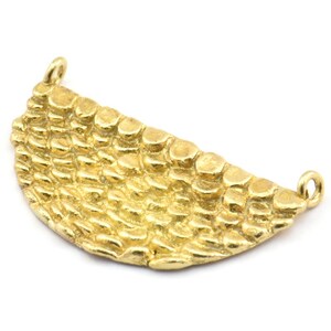 May include: A gold-colored, half-moon shaped jewelry component with a textured surface. The pendant has a series of small, raised, circular details across its surface. Two small loops are at each end for attaching to other jewelry pieces.