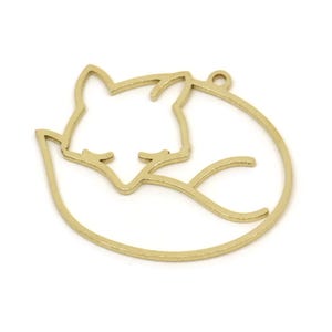 May include: A gold-colored metal charm in the shape of a sleeping fox. The fox is curled up inside a circular frame, with a small loop at the top for hanging. The charm is likely used for jewelry making or other crafts.
