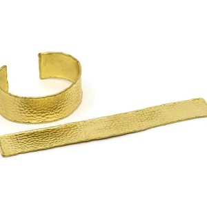 May include: A set of two gold-toned hammered metal bracelets. One bracelet is a wide cuff and the other is a thin, flat band.