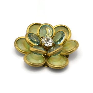 May include: A gold-toned flower brooch with green and clear rhinestones. The center of the flower has a larger, clear rhinestone.