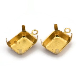 Puede incluir: Dos engastes de metal dorado para una piedra preciosa de forma cuadrada. Cada engaste tiene un pequeño bucle en la parte superior para sujetar una cadena o una cuerda.
