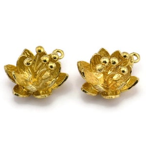 Puede incluir: Dos abalorios de metal dorado en forma de flor con un bucle para sujetar a joyas u otras manualidades. Las flores tienen un diseño detallado y un acabado texturizado.