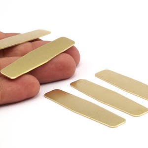 Puede incluir: Cinco placas rectangulares de metal de color dorado, algunas ligeramente redondeadas en las esquinas, est&aacute;n dispuestas sobre una superficie blanca.