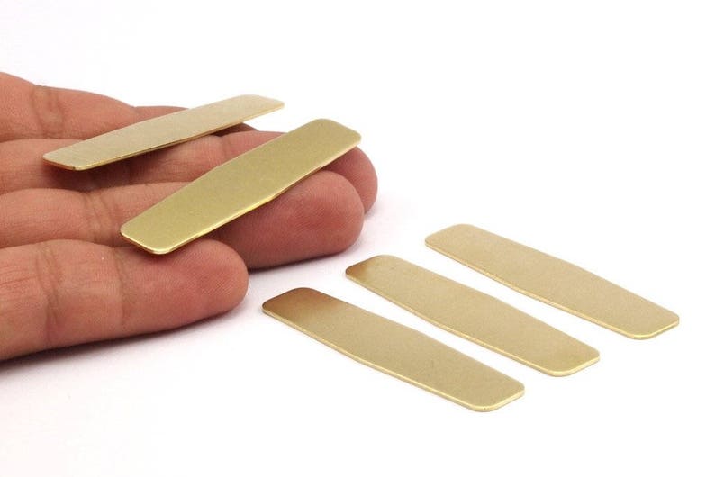 Puede incluir: Cinco placas rectangulares de metal de color dorado, algunas ligeramente redondeadas en las esquinas, est&aacute;n dispuestas sobre una superficie blanca.