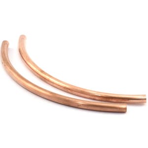May include: Two copper pipe segments, each bent into a gentle arc, are arranged side-by-side. The pipes are a warm, reddish-brown color and have a smooth, polished finish.
