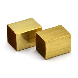Puede incluir: Dos bloques cuadrados macizos de lat&oacute;n, cada uno con una superficie lisa y pulida. Los bloques son de tama&ntilde;os ligeramente diferentes y est&aacute;n colocados uno al lado del otro.