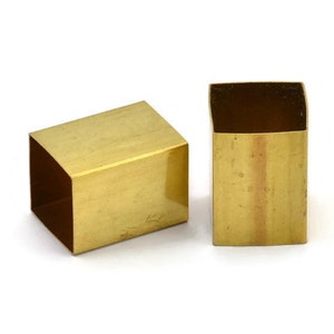 Puede incluir: Dos tubos cuadrados de metal de color dorado. Los tubos son huecos y tienen un acabado liso y pulido.