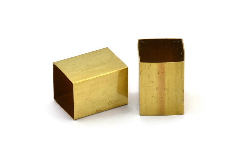 Puede incluir: Dos tubos cuadrados de metal de color dorado. Los tubos son huecos y tienen un acabado liso y pulido.