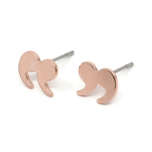 May include: A pair of rose gold-colored stud earrings shaped like quotation marks. The earrings have a smooth, metallic finish and are set against a white background. The posts are silver-colored.