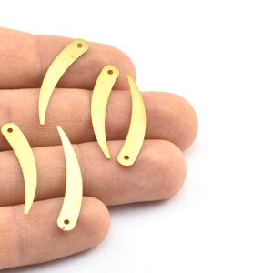 May include: Five gold-colored metal charms shaped like a curved fang with a hole at the top.