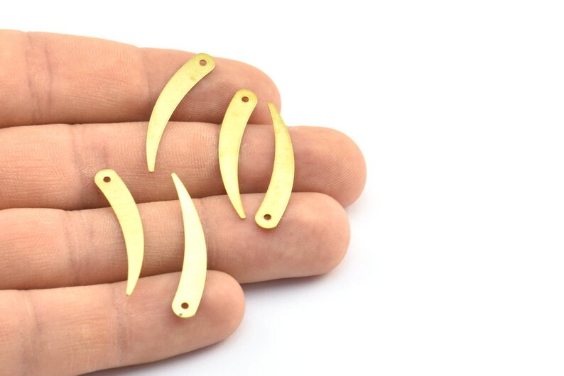 May include: Five gold-colored metal charms shaped like a curved fang with a hole at the top.
