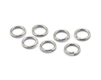 May include: Seven silver jump rings, also known as split rings, are arranged on a white surface. These rings are commonly used in jewelry making and crafting.