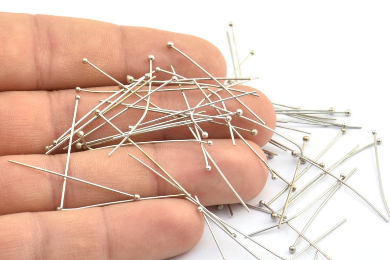 May include: A close-up of a hand holding a large quantity of silver-toned straight pins with round heads.