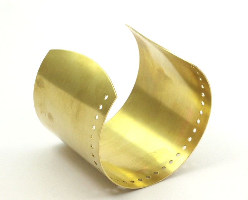 K&ouml;nnte beinhalten: Ein goldfarbenes Metall-Armband mit glatter, polierter Oberfl&auml;che. Das Armband hat eine Reihe kleiner L&ouml;cher entlang der Kante.