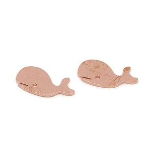 May include: Two rose gold whale-shaped charms. Each charm features a small hole and a tail fin. The charms are designed with a simple, minimalist aesthetic, perfect for jewelry making or crafting projects.