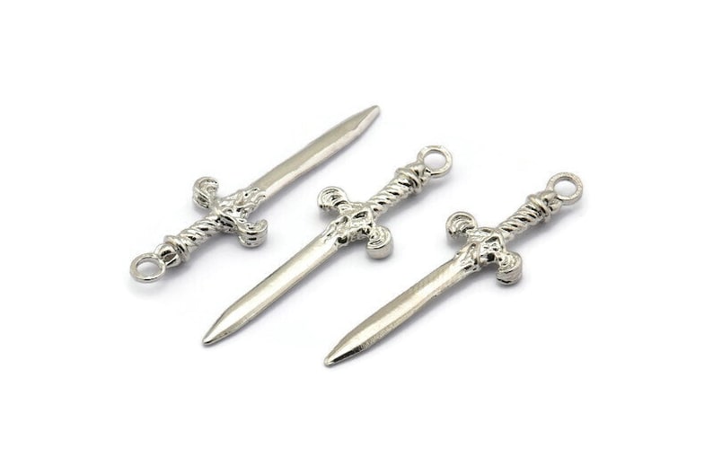 May include: Three silver sword charms with intricate details. The swords have a twisted design and a pointed tip.