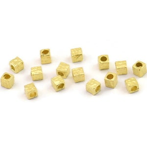 May include: A group of 15 gold-coloured metal square beads with a hole in the centre. The beads have a hammered texture.