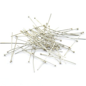 May include: A pile of silver head pins with round heads. The pins are scattered on a white background.