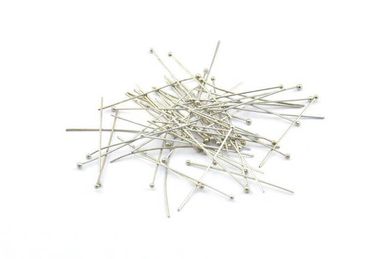 May include: A pile of silver head pins with round heads. The pins are scattered on a white background.