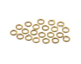 May include: A group of 20 gold jump rings, a type of jewelry finding, are scattered on a white background.