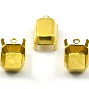 May include: Three gold-toned metal settings for bezel settings. Each setting has a square shape with rounded corners and a small loop at the top for attaching a pendant or charm.