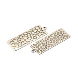 May include: Two silver-toned metal rectangular pendant charms with a textured surface resembling a reptile skin pattern.