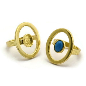 Puede incluir: Dos anillos de oro con un diseño circular. Un anillo tiene una piedra preciosa azul en el centro, mientras que el otro anillo tiene un círculo más pequeño y vacío en el centro.