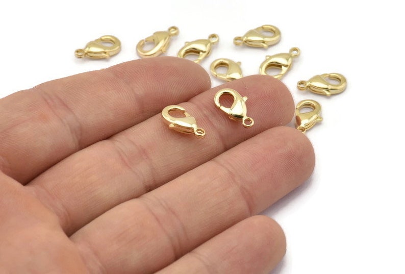 Peut inclure: Gros plan sur un groupe de fermoirs &agrave; ressort en m&eacute;tal dor&eacute;. Les fermoirs sont petits et d&eacute;licats, et ils sont parfaits pour ajouter une touche d'&eacute;l&eacute;gance aux bijoux.